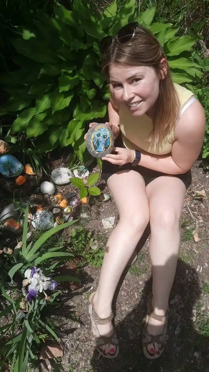 Une femme montre une pierre peinte dans un jardin.